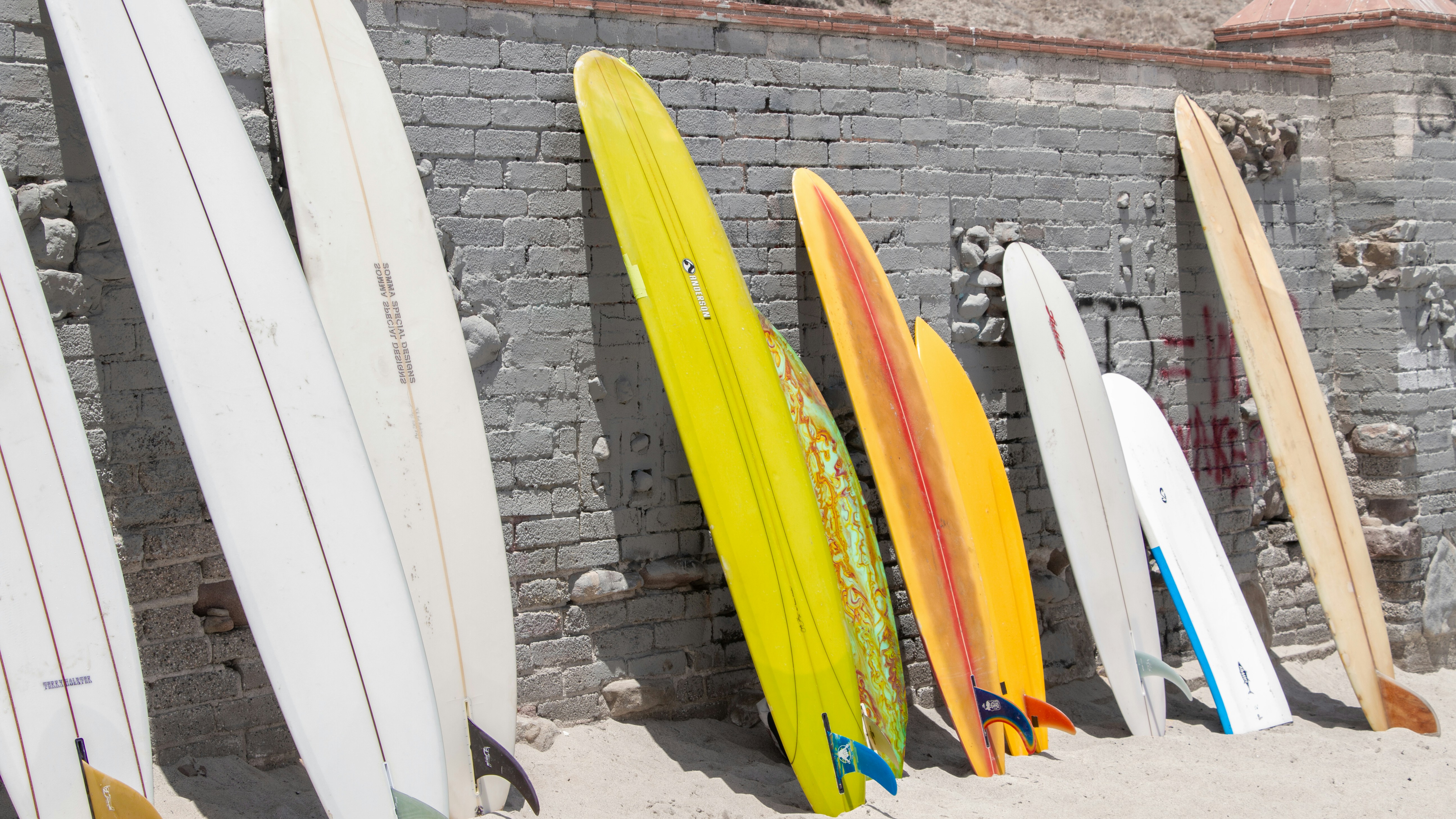 Yellow and blue surfboard leaning against a white wall, representing the California beach college lifestyle